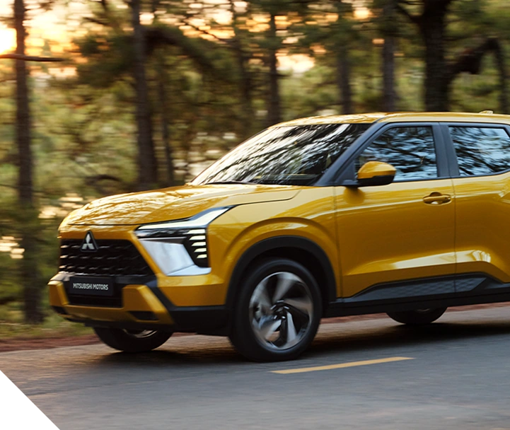 Mitsubishi amarillo circulando por un camino rodeado de árboles.